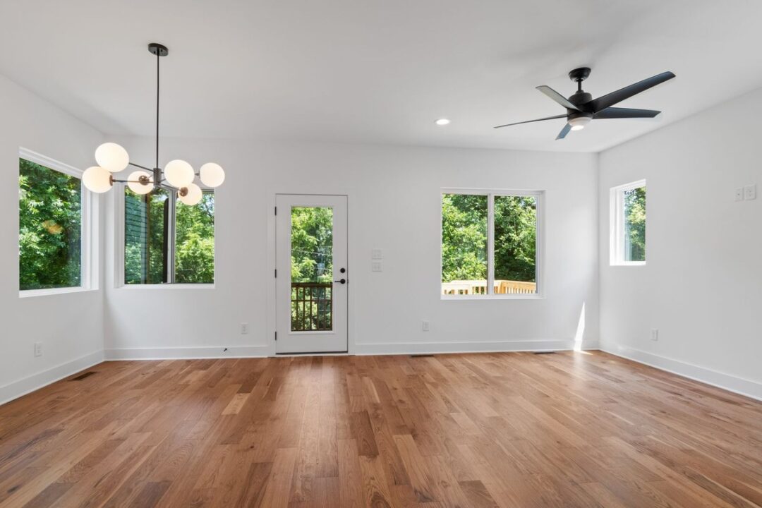 Empty bright living room with hardwood floors, globe chandelier, and glass door to a deck