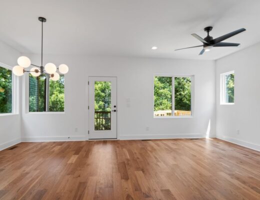 Empty bright living room with hardwood floors, globe chandelier, and glass door to a deck