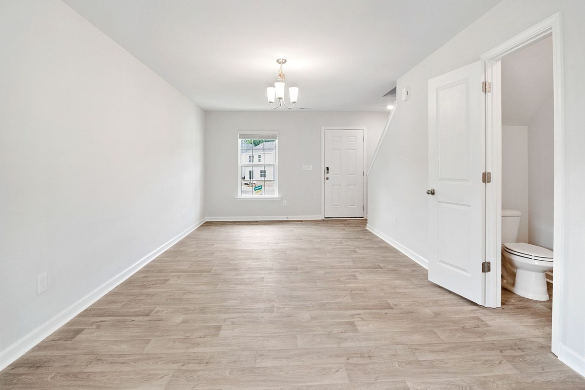 Empty new-home living area with light wood flooring, chandelier, and open door to a powder room under stairs